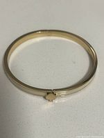 Front view of gold tone bangle bracelet with spade clasp.
