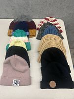 Photo showing front view of 14 wool and knit hats arranged in two rows on a white table against a gray background.