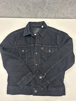 Front view of black Levi's denim jacket laid flat on a surface showing button-up design, chest pockets, and overall good condition.
