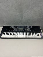 Front view of black Rockjam electronic keyboard showing full 54 keys, speaker grills, and control panel with LCD screen and buttons.