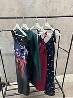 Four women's dresses on a black metal clothing rack against a concrete wall, showing styles and colors.