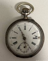 Front view of the silver pocket watch showing the white dial with black Roman numerals and ornate hands, including a small seconds subdial at 6 o'clock.