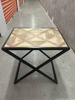 Front angled view of table showing wooden patterned top and metal X-shaped cross legs.