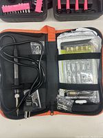 Soldering iron and accessories inside an orange and black zippered case including soldering iron, stand, multiple tips and small screwdrivers