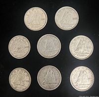 Top view of eight early Canadian silver dimes featuring the Bluenose schooner design scattered on black background showing dates 1913, 1926, 1936 and others.
