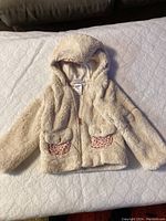 Cream colored, plush faux fur toddler jacket with hood and two pink leopard print-lined front pockets, zip closure.