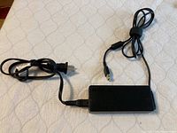 Full view of Lenovo 90W 20V AC adapter with power cord coiled beside it on a beige patterned surface.