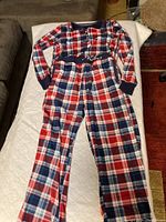 Full view of the Nautica plaid sleepwear laid flat on a bed, showing top and pants with red, white, and blue plaid pattern.