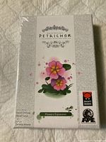 Front view of Petrichor Flowers Expansion box with floral artwork and logos of Mighty Boards and APE Games visible.