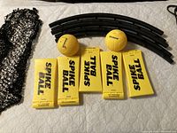Black curved frame legs, two yellow Spikeball balls, four yellow base pads, and black net laid out on a bed.