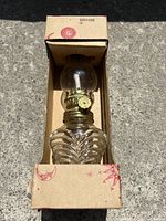 Miniature coal oil lamp with ribbed clear glass base inside original cardboard box with red patterns