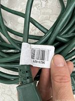 Close-up photo showing green 80-foot electrical extension cord plug with barcode label attached.