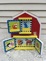 Front view of the barn toy showing colorful animal pictures behind doors including a cow, sheep, horse, blue bug, squirrel, and lion.