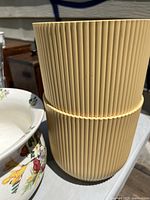 Two vertically ridged light brown wooden canisters stacked one on top of the other.
