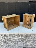 Two rustic pine wood crates displayed against black backdrop on concrete floor, one crate laid on side showing open rectangular interior, other upright