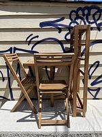Folded state of the teak-colored wooden table and two chairs set leaning against a wall with graffiti.