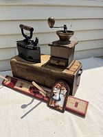 View of the coal iron closed beside the coffee grinder and pine box drawer with additional small country-themed decorations.