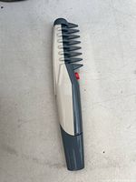 Electric dog grooming comb showing front profile with teeth, red switch button, and sleek plastic body.
