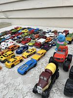 Wide view of die cast cars and trucks arranged on a table showing multiple rows and a few Thomas Tank Engine toy figures prominently at the front