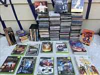 Full shot showing stacks of CDs, video games, and 8-track tapes arranged on a table outdoors against a wooden wall.