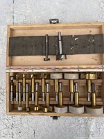 Open wooden box showing the set of 17 brass and steel Forstner drill bits lined up with foam holders in the lid.