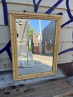 Full view of the rectangular mirror with bamboo frame, reflecting outdoor alleyway.