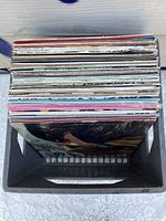 Top view of black plastic milk crate filled with 18 vinyl LP records showing album cover edges.