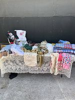 Overview of mixed vintage textiles including lace fabric and printed aprons on a table with black backdrop