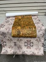 Full view of two rolls of wallpaper laid out on a surface showing the bicycle-themed roll on top of the extra wide purple floral patterned roll.