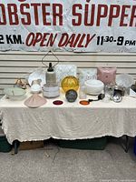 Full view of vintage lighting lot including multiple glass and metal shades and the Aladdin marbleized lamp base on beige tablecloth