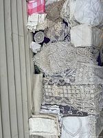 Photo showing a variety of vintage white and cream lace and linen pieces spread out, including doilies, collars, embroidered linens, and some plain fabrics all layered and overlapping.