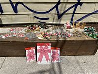 Wide shot of varied vintage Christmas ornament lot on wooden surface, includes bows, small straw ornaments, holly greenery, and assorted decorative ribbons.