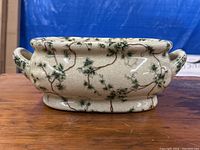 Side view of the oval ceramic jardiniere with green floral vine pattern and handles, showing crackled glaze texture.