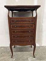 Front view of antique music cabinet showing five drawers with decorative inlay and curved legs.