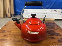 Front view of red enamel Le Creuset kettle with spout whistle and handle on wooden surface.