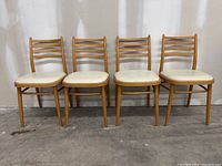 Front view of four vintage mid-century dining chairs in blonde wood with ladder backs and cream upholstered seats, showing general condition and style.