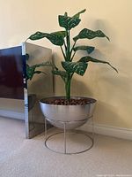 Overall straight-on view of planter bowl, stand and artificial plant against wall