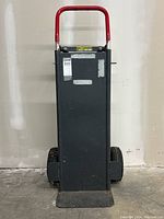 Front view of moving dolly showing red handle, black metal base, and large tires.