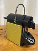 Front angle view of Nespresso coffee machine showing yellow textured side panel, black body, chrome handle, spout and drip tray.