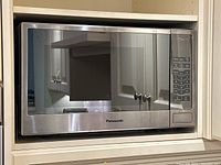 Front view of the Panasonic stainless steel microwave displaying the reflective glass door and keypad.