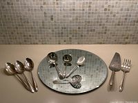 Round mirror beneath assorted serving pieces: ladles, sugar spoon, slotted spoon