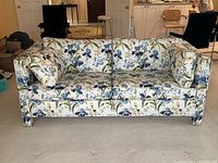 Front view of sofa showing two seat cushions, two loose arm pillows, floral print upholstery on beige carpet
