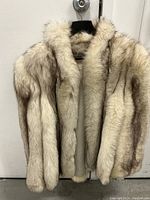 Front view of full-length fox fur coat hanging on black hanger against white door