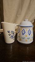 Front view of ceramic milk jug with blue rose floral design and cookie jar with colorful geometric patterns.