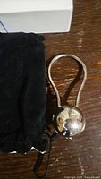 Silver plated baby rattle placed next to a black velvet pouch on a wooden surface.