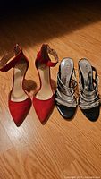 Photo showing both pairs of ladies heeled sandals on wooden floor, Vincent Camuto red suede and White House Black Market black/white multi-strap.