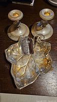 Silver candy dish shaped like a leaf with decorative handle, sitting alongside two silver candle holders on a dark wooden surface.