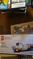 Photo showing OXO branded winged corkscrew in original blister packaging and Pfaltzgraff Slate serving board box showing a 7-piece set including the slate board and markers.