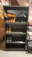 Full view of the black wooden shoe rack with slanted shelves holding boots, sneakers, and bags for scale. Shoes not included in sale.