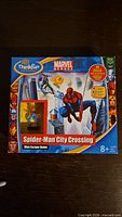 Front view of the game box showing ThinkFun and Marvel Heroes branding plus Spider-Man graphics and the title 'Spider-Man City Crossing Web Escape Game', age recommendation 8+.